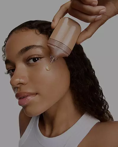 Modella che si applica una goccia di evidenziatore liquido Lancome sulla guancia.