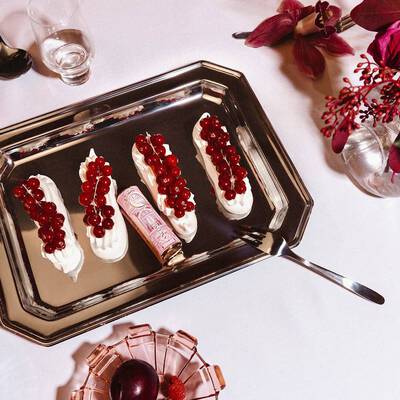 Un rossetto Lancome incastonato tra quattro dessert con crema guarniti con ribes rossi su un vassoio d'argento.