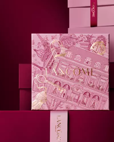 Una pila elegante di scatole regalo Lancome rosa e bordeaux intenso, con una scatola centrale decorata con illustrazioni architettoniche parigine dorate.