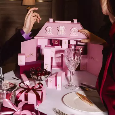 Le mani che interagiscono con un calendario dell'avvento rosa Lancome su un tavolo da pranzo festoso con stoviglie e ciliegie.