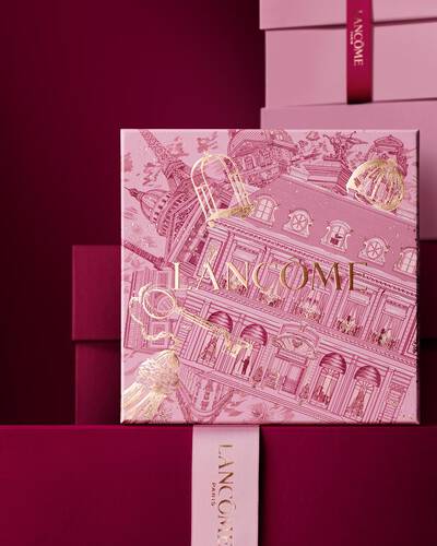 Una pila elegante di scatole regalo Lancome rosa e bordeaux intenso, con una scatola centrale decorata con illustrazioni architettoniche parigine dorate.