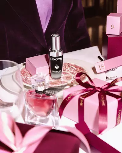 Prodotti di bellezza Lancome e scatole regalo rosa disposte su un tavolo da pranzo festoso.