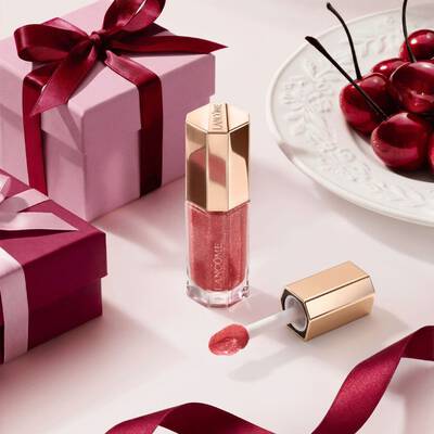 Lucidalabbra color bacca Lancome in un tubo esagonale di lusso, decorato con scatole regalo e ciliegie.