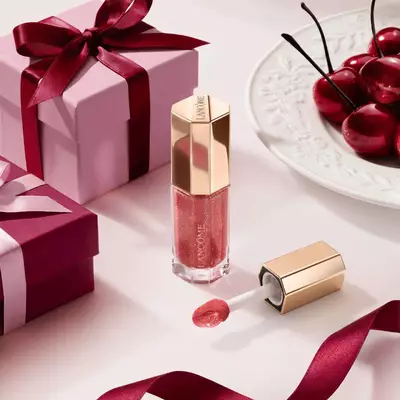 Lucidalabbra color bacca Lancome in un tubo esagonale di lusso, decorato con scatole regalo e ciliegie.