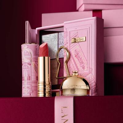 Un set regalo natalizio Lancome selezionato con rossetto, palette di ombretti e prodotti di bellezza dorati esposti su una custodia rosa decorativa.