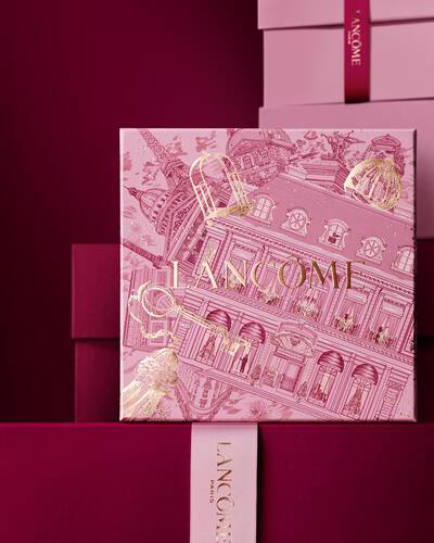Immagine della scatola regalo rosa Lancome per le festivita davanti a una pila di scatole regalo rosa e rosso scuro, su uno sfondo rosso scuro.