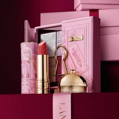 Un set regalo natalizio Lancome selezionato con rossetto, palette di ombretti e prodotti di bellezza dorati esposti su una custodia rosa decorativa.