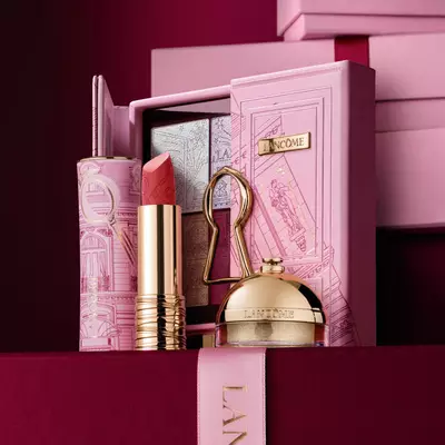 Un set regalo natalizio Lancome selezionato con rossetto, palette di ombretti e prodotti di bellezza dorati esposti su una custodia rosa decorativa.