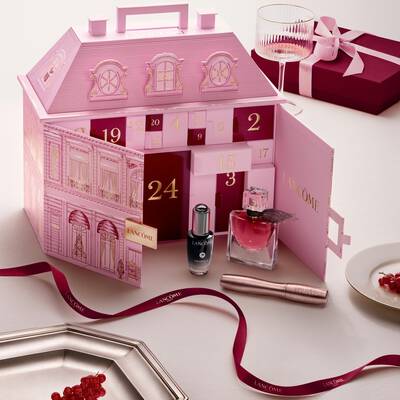 Un calendario dell'avvento rosa aperto di Lancome per la casa a schiera esposto con prodotti di bellezza e un nastro rosso.
