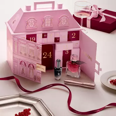 Un calendario dell'avvento rosa aperto di Lancome per la casa a schiera esposto con prodotti di bellezza e un nastro rosso.