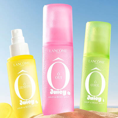 Due bottiglie rosa, una bottiglia rettangolare di profumo con un disegno testurizzato e una bottiglia spray, ferma su una spiaggia sabbiosa. Un asciugamano da spiaggia rosa a righe piegato e accanto alle bottiglie. Sullo sfondo c'e un cielo azzurro limpido e l'oceano.