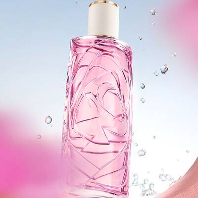 Una bottiglia di profumo rosa chiaro con un disegno di vetro testurizzato, su uno sfondo azzurro chiaro, con gocce d'acqua che schizzavano intorno. La bottiglia si vede attraverso un'apertura circolare in una parete rosa testurizzata, e ci sono fiori rosa sfocati in primo piano e sullo sfondo.