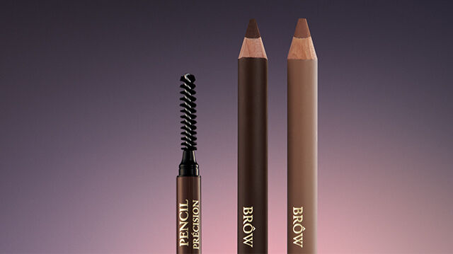 Three eyebrow pencils are displayed against a gradient background, featuring a spoolie brush on the left, with two brown pencils on the right.