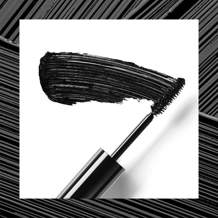 A close-up of a mascara wand with a bold black stroke of mascara against a white background.
