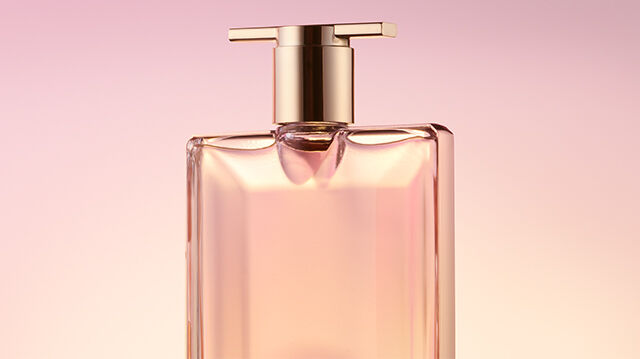 A sleek, elegant perfume bottle with a gold cap, set against a soft pink background.