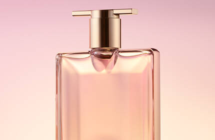 A sleek, elegant perfume bottle with a gold cap, set against a soft pink background.
