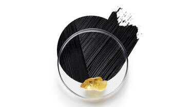 A petri dish containing a golden substance next to a circular black stroke, resembling artistic paint.