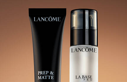 Two Lancome makeup products are displayed: a black tube labeled "Prep & Matte" and a clear bottle labeled "La Base Pro." Both are set against a warm, gradient background.