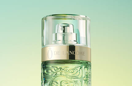 A close-up of a green glass perfume bottle with a silver and gold pump, set against a gradient background of soft green and yellow hues.