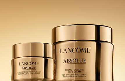 A gradient gold background featuring two jars of Lancome Absolue skincare products, one large and one small, both with sleek golden lids.