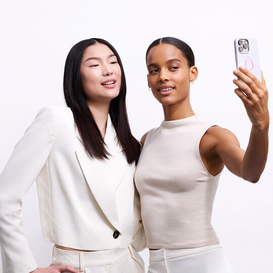 Due donne in abiti bianchi scattano un selfie con uno smartphone.
