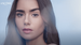 A close-up of a young woman with long, dark hair and natural makeup, looking directly at the camera with a soft expression. The image features a light blue background and includes the text "LANCOME PARIS" in the corner.