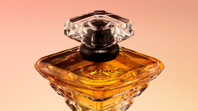 A close-up of an elegant perfume bottle with a diamond-shaped stopper, showcasing a rich amber liquid against a soft gradient background.