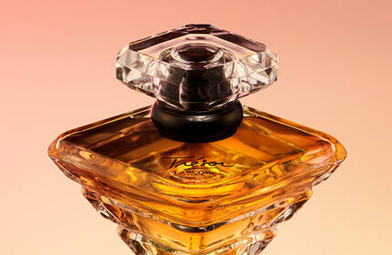 A close-up of an elegant perfume bottle with a diamond-shaped stopper, showcasing a rich amber liquid against a soft gradient background.