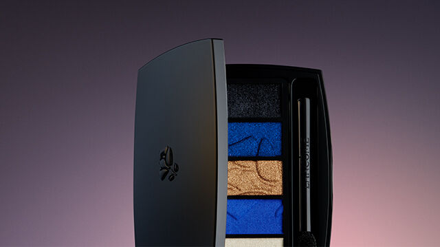 A sleek, closed makeup palette displaying vibrant blue, gold, and black eyeshadow colors, set against a softly lit gradient background.