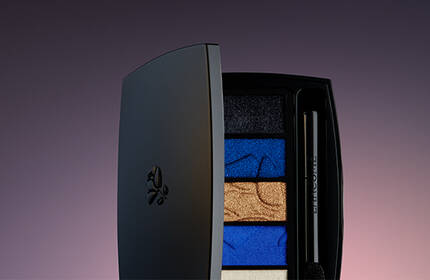 A sleek, closed makeup palette displaying vibrant blue, gold, and black eyeshadow colors, set against a softly lit gradient background.