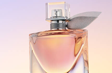 A close-up of an elegant perfume bottle with a sleek design, featuring a clear cap and a decorative leaf-like accent, against a soft gradient background.