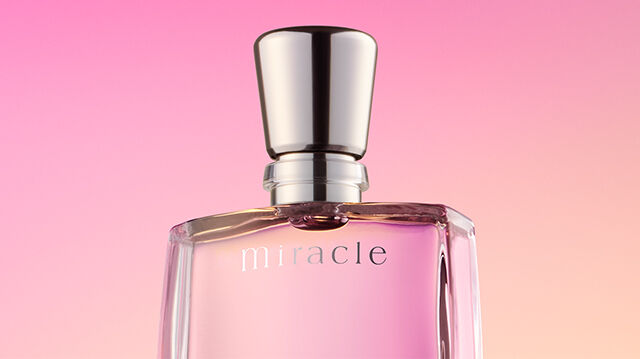 A clear glass perfume bottle labeled "Miracle" with a silver cap against a soft gradient background of pink and purple hues.