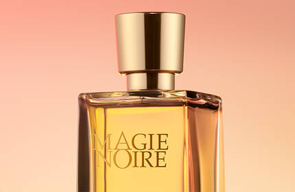 A close-up of a perfume bottle with a golden cap, set against a soft gradient background of warm colors.