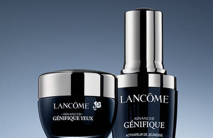 A visually appealing arrangement of two Lancome skincare products against a gradient blue background. The products include a small jar and a sleek serum bottle, both featuring elegant packaging.