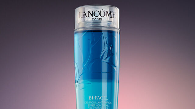 A sleek, cylindrical bottle of Lancome skincare product with a gradient of blue liquid, set against a dark, softly lit background.
