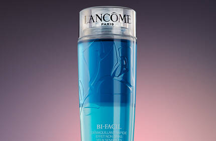 A sleek, cylindrical bottle of Lancome skincare product with a gradient of blue liquid, set against a dark, softly lit background.