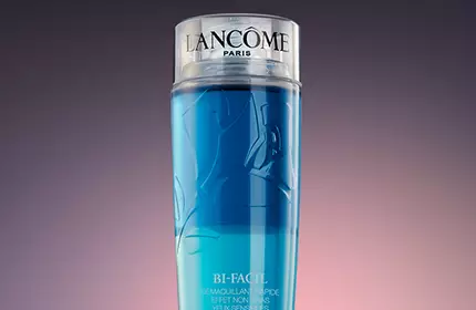 A sleek, cylindrical bottle of Lancome skincare product with a gradient of blue liquid, set against a dark, softly lit background.