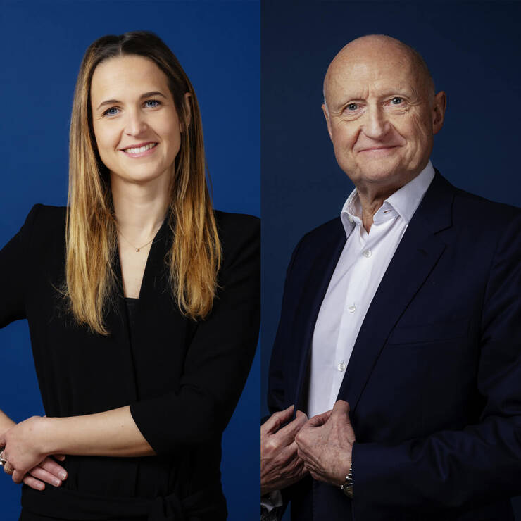 Due persone sorridenti, una donna con capelli lunghi e un uomo maturo, davanti a uno sfondo blu.