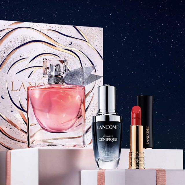 Immagine che mostra confezioni regalo di prodotti Lancome, tra cui un profumo e cosmetici, su uno sfondo stellato.