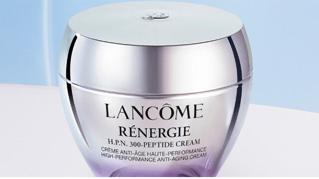 Two purple skincare jars from Lancome are displayed against a soft gradient background, showcasing their sleek design and branding.