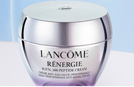 Two purple skincare jars from Lancome are displayed against a soft gradient background, showcasing their sleek design and branding.