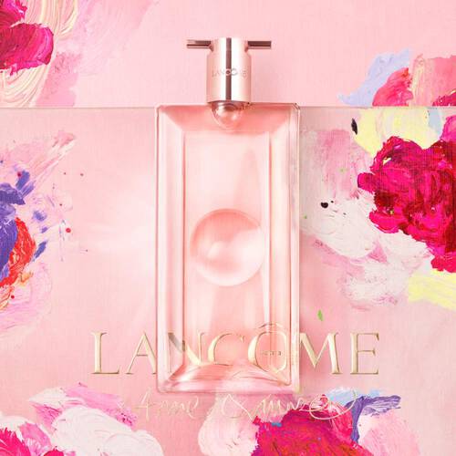 Flacone di profumo Lancome su sfondo rosa con fiori colorati, elegante e femminile.
