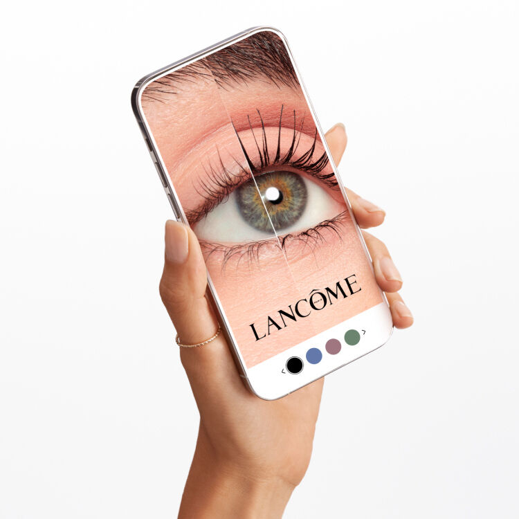 Una mano che tiene uno smartphone con un'immagine ingrandita di un occhio, mostrante un mascara Lancome.