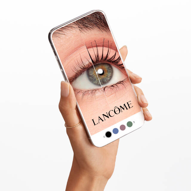 Una mano che tiene uno smartphone con un'immagine ingrandita di un occhio, mostrante un mascara Lancome.