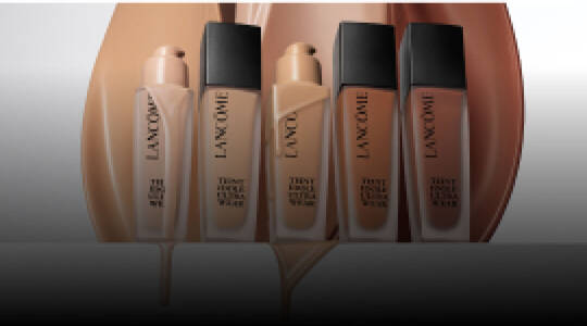 Immagine che mostra diversi flaconi di fondotinta Lancome su uno sfondo sfumato.