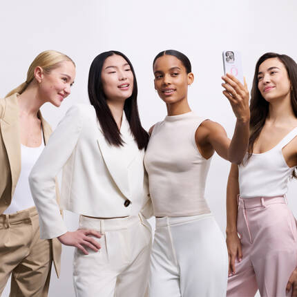 Quattro donne sorridenti si prendono una selfie, indossando abiti eleganti in tonalita chiare.