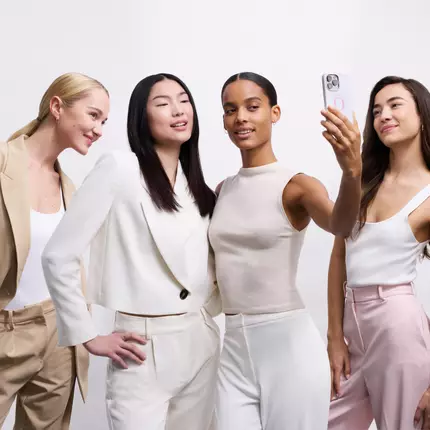 Quattro donne sorridenti si prendono una selfie, indossando abiti eleganti in tonalita chiare.