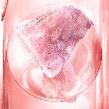 Un cristallo rosa brillante posizionato su una superficie lucida, circondato da riflessi luminosi e sfumature rosa.