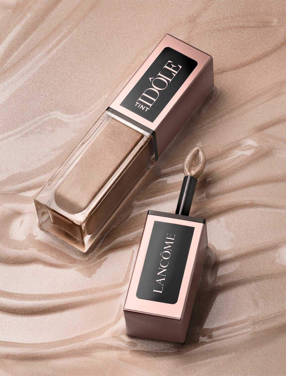 Un flacone di tinta per labbra Lancome nella tonalita dorata, appoggiato su una superficie scintillante e dorata.