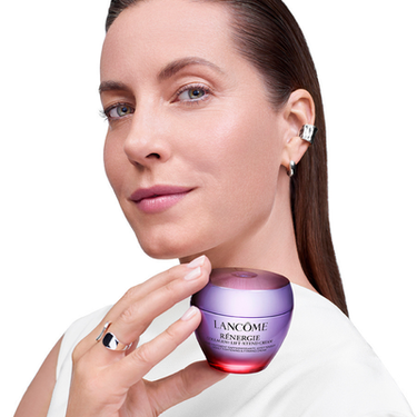Innovazione Beauty Tech Lancome: modella con pelle radiosa davanti a un dispositivo di analisi della pelle professionale su sfondo dorato.